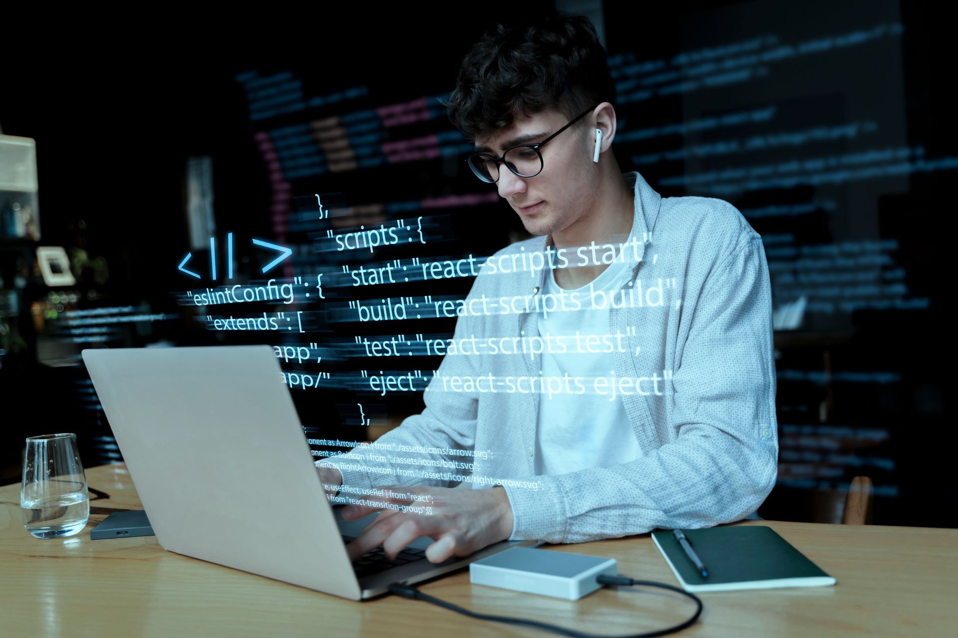 Young person with glasses working on laptop, code overlay, indoors.